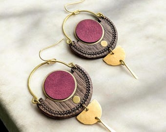 May include: A pair of gold hoop earrings with a wooden crescent moon design. The crescent moon is decorated with a burgundy circle and a gold dot. The earrings have a gold dangle with a half-circle shape.