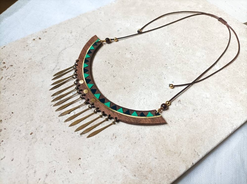 May include: A wooden statement necklace with a geometric design in green, black, and gold. The necklace has a fringe of gold metal accents.