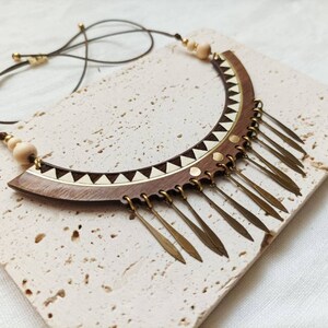 May include: A wooden and brass necklace with a geometric design and a fringe of brass pendants.