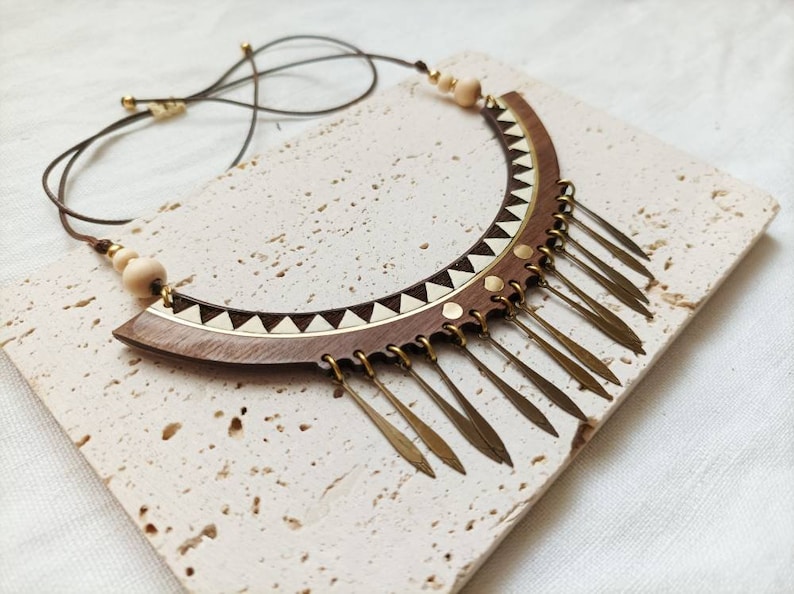 May include: A wooden and brass necklace with a geometric design and a fringe of brass pendants.