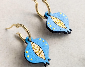 Può includere: Orecchini a cerchio dorati con ciondoli a forma di melograno in legno blu. I melograni hanno un design a semi bianchi e gialli e dettagli a pois gialli. Un accessorio unico e colorato.