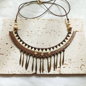 May include: A wooden statement necklace with a brown and white geometric pattern and a fringe of gold-toned metal accents.
