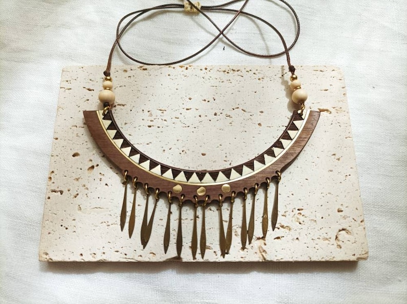 May include: A wooden statement necklace with a brown and white geometric pattern and a fringe of gold-toned metal accents.
