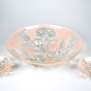 May include: A set of three glass bowls with a pink tint and a raised floral design. The bowls are in different sizes and are perfect for serving snacks or desserts.