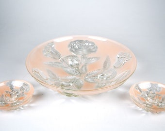 May include: A set of three glass bowls with a pink tint and a raised floral design. The bowls are in different sizes and are perfect for serving snacks or desserts.
