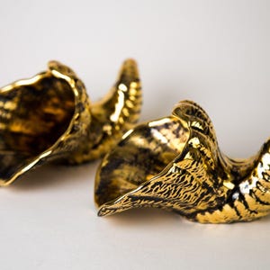 May include: Two decorative, gold-colored, horn-shaped objects with a textured surface. The horns have a glossy finish and are set against a white background. The horns are likely used for decorative purposes.