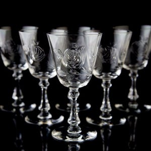 May include: Six clear glass wine glasses with a floral etched design. The glasses are arranged in a row on a black background.