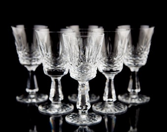 Puede incluir: Juego de seis copas de vino de cristal transparente con diseño de vidrio tallado. Las copas están dispuestas en fila sobre un fondo negro.