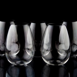 May include: Five clear glass wine glasses on a black background. The glasses are all the same shape and size, and they are arranged in a row.