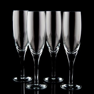 May include: Four clear glass champagne flutes on a black background. The flutes are empty and have a classic design.