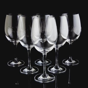 May include: A collection of clear wine glasses arranged on a black surface. The glasses have a classic design with a rounded bowl and a long stem. The image is well-lit, highlighting the transparency of the glass.