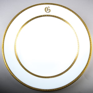 May include: White porcelain dinner plate with a gold rim and a gold initial "G" in the center.
