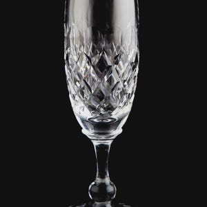 Könnte beinhalten: Klare Kristall-Champagnerflöte mit Diamantschliffmuster auf der Schale. Der Stiel hat einen bauchigen Mittelteil und einen kreisförmigen Fuß. Das Glas ist für Sekt oder Champagner bestimmt.
