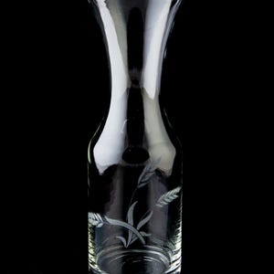 Peut inclure: Une carafe en verre transparent avec un motif gravé de tiges de blé. La carafe a une large ouverture et un col étroit.