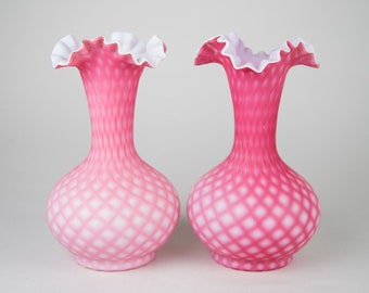 May include: Two pink and white milk glass vases with ruffled tops and a diamond pattern. The vases are a light pink color with a white overlay.