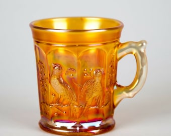 May include: A vintage amber glass cup with a clear handle. The cup has a raised design of birds on branches.