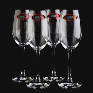 May include: A set of five clear wine glasses with long stems and wide bowls. Each glass has a red and black oval sticker near the top. The glasses are arranged in a row against a black background.