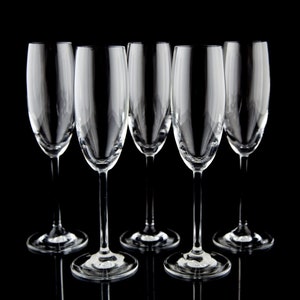 May include: Five clear glass champagne flutes arranged in a row on a black background.