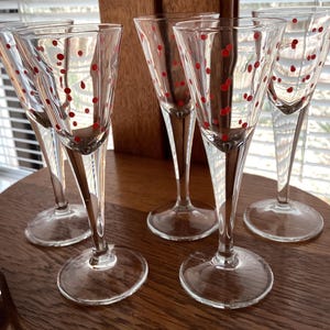 May include: Set of six clear glass shot glasses with red polka dots. The glasses have a tall, slender stem and a wide, round base.