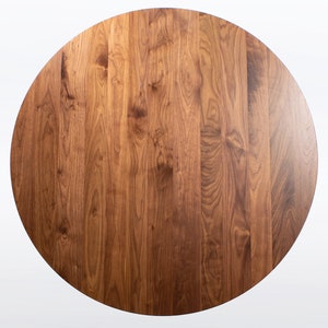 This is a view looking straight down at the round dining table handmade in solid walnut wood. This table has a pedestal base with four curved legs connected at the center. The look of the table is midcentury modern, Danish modern and Scandinavian.