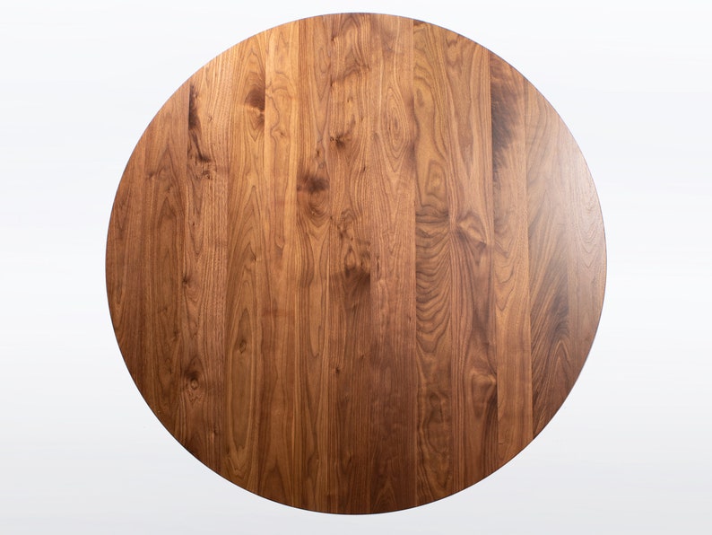 This is a view looking straight down at the round dining table handmade in solid walnut wood. This table has a pedestal base with four curved legs connected at the center. The look of the table is midcentury modern, Danish modern and Scandinavian.