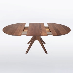 A modern round extendable dining table hand crafted in solid walnut wood.