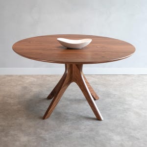 Modern round dining table in solid walnut wood with sleek finish, featuring an elegant four-legged pedestal base design. Ideal for contemporary dining room settings.
