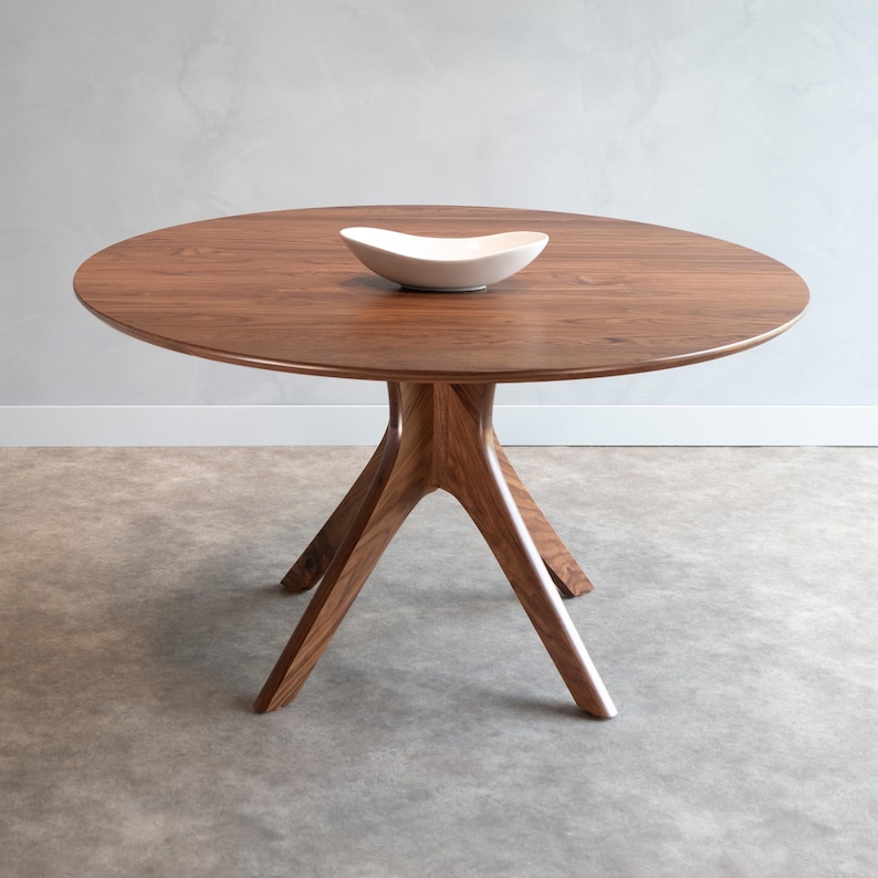 Modern round dining table in solid walnut wood with sleek finish, featuring an elegant four-legged pedestal base design. Ideal for contemporary dining room settings.