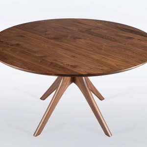 Modern round dining table in solid walnut wood with sleek finish, featuring an elegant four-legged pedestal base design. Ideal for contemporary dining room settings.