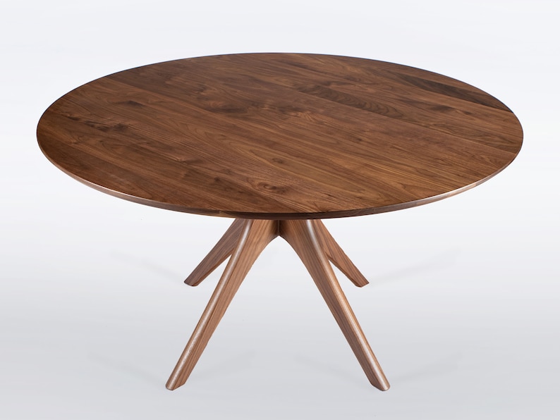 Modern round dining table in solid walnut wood with sleek finish, featuring an elegant four-legged pedestal base design. Ideal for contemporary dining room settings.