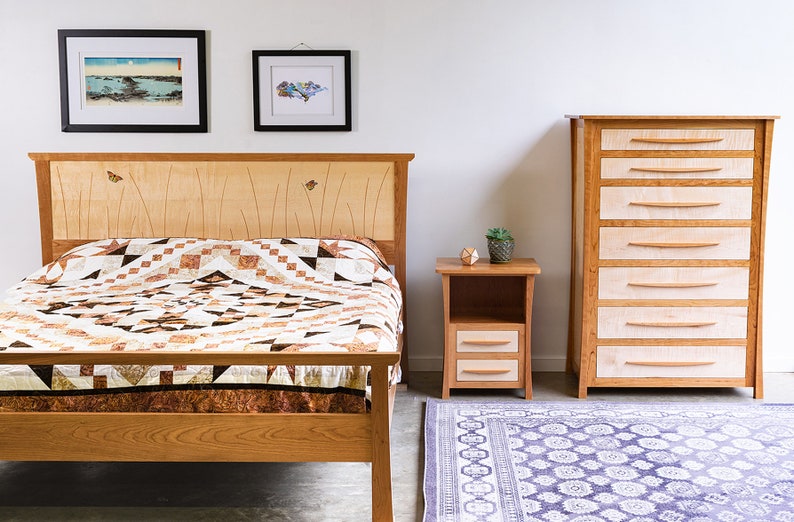 May include: A bedroom set with a wooden bed frame, a nightstand, and a dresser. The bed has a brown and white quilt and a wooden headboard with butterfly inlays. The nightstand has two drawers and the dresser has six drawers. The room has a white wall and a patterned rug.