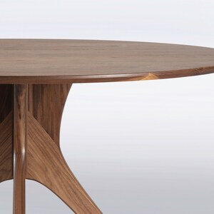 Modern round dining table in solid walnut wood with sleek finish, featuring an elegant four-legged pedestal base design. Ideal for contemporary dining room settings.