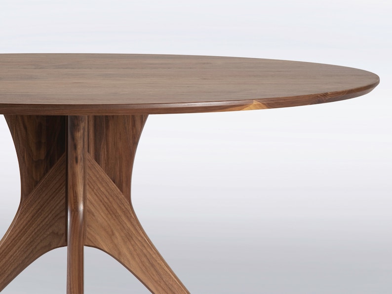 Modern round dining table in solid walnut wood with sleek finish, featuring an elegant four-legged pedestal base design. Ideal for contemporary dining room settings.