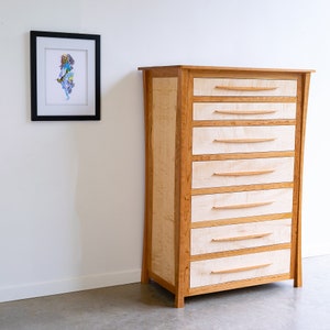 May include: A tall wooden dresser with six drawers. The dresser is made of light wood with a natural finish. The drawers have simple, curved wooden handles.