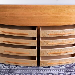 May include: A wooden dresser with six drawers on each side. The drawers are open and have a light wood finish. The dresser is on a patterned rug.