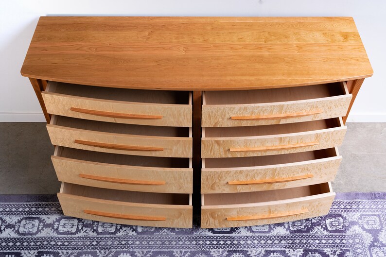 May include: A wooden dresser with six drawers on each side. The drawers are open and have a light wood finish. The dresser is on a patterned rug.