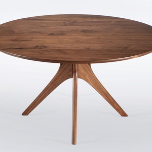Round dining table handmade in solid walnut wood. This table has a pedestal base with four curved legs connected at the center. The look of the table is midcentury modern, Danish modern and Scandinavian.  The table available in a variety of sizes.