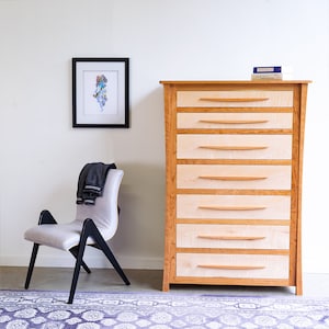 May include: A light wood dresser with six drawers and a simple design. The dresser is made of natural wood with a light finish. The drawers have a slightly curved handle.