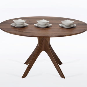 Round dining table handmade in solid walnut wood. This table has a pedestal base with four curved legs connected at the center. The look of the table is midcentury modern, Danish modern and Scandinavian.  The table available in a variety of sizes.