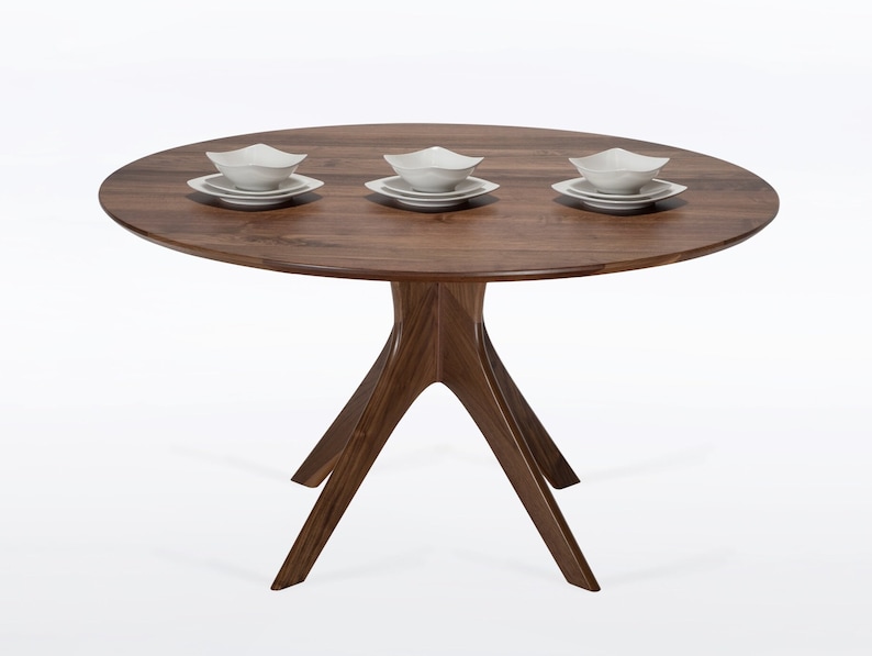 Round dining table handmade in solid walnut wood. This table has a pedestal base with four curved legs connected at the center. The look of the table is midcentury modern, Danish modern and Scandinavian.  The table available in a variety of sizes.