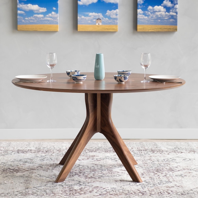 Modern round dining table in solid walnut wood with sleek finish, featuring an elegant four-legged pedestal base design. Ideal for contemporary dining room settings.