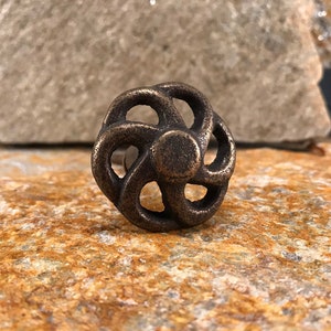 May include: A bronze-coloured metal cabinet knob with a decorative, swirling, circular design.