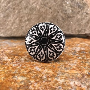 May include: A white ceramic knob with a black and white mandala design. The knob is round and has a raised edge.