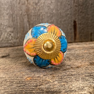 May include: A white ceramic knob with a floral design. The knob features blue, yellow, and pink petals with gold accents. The knob is perfect for adding a touch of vintage charm to any room.