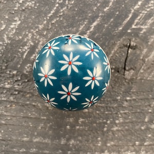 May include: A teal blue round knob with a white daisy pattern and red centres.