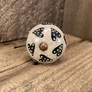 May include: A white ceramic knob with black and white polka dot hearts. The knob has a distressed look and a copper colored screw.
