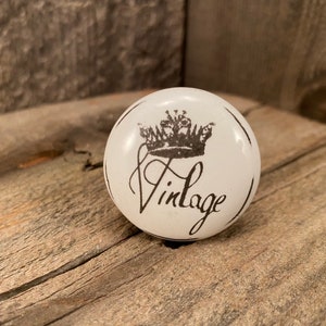 May include: White ceramic knob with a black crown and the word "Vintage" written in cursive.