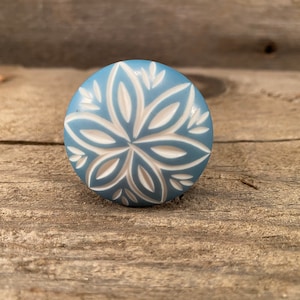 以下が含まれることがあります： 白い花の模様が施された青いセラミック製のノブ。ノブは丸く、表面は滑らかです。