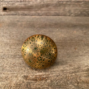 Könnte beinhalten: Ein runder Knopf in Gold mit einem grünen und goldenen Blumenmuster.