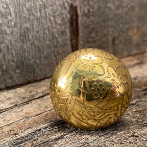 Könnte beinhalten: Ein goldfarbener Metallknopf mit floralem Design. Der Knopf hat eine glänzende, polierte Oberfläche und zeigt komplizierte Details von Blumen und Blättern.